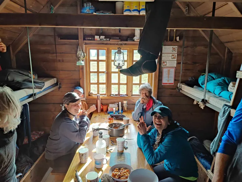 Hikers sharing a meal around a wooden table between bunks inside Þjófadalir hut