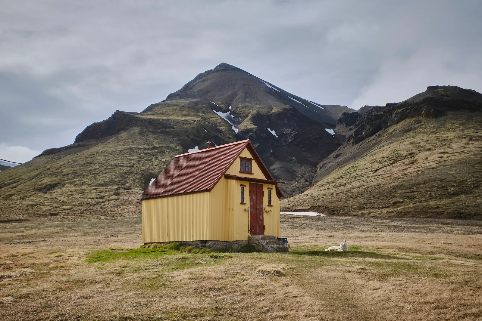 A small yellow mountain hut beneath rugged Highland slopes