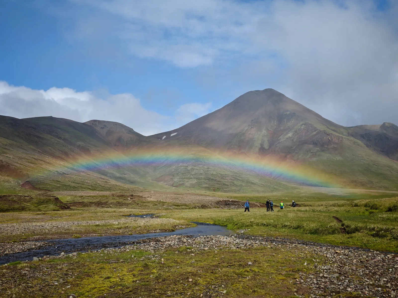 A rainbow over hikers crossing a green Highland valley