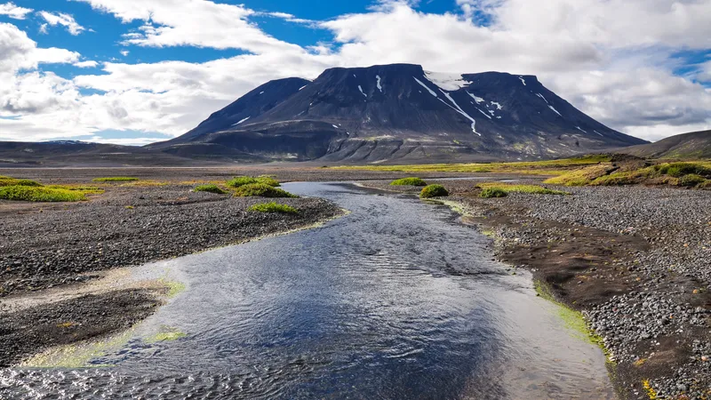 A clear river winding between gravel banks beneath a broad, snow-streaked Highland mountain