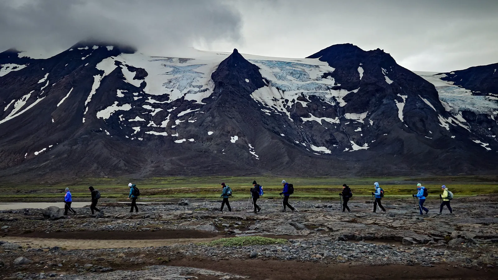 Ancient Trails hikers walking across open rocky ground below Hrútfell and its glacier