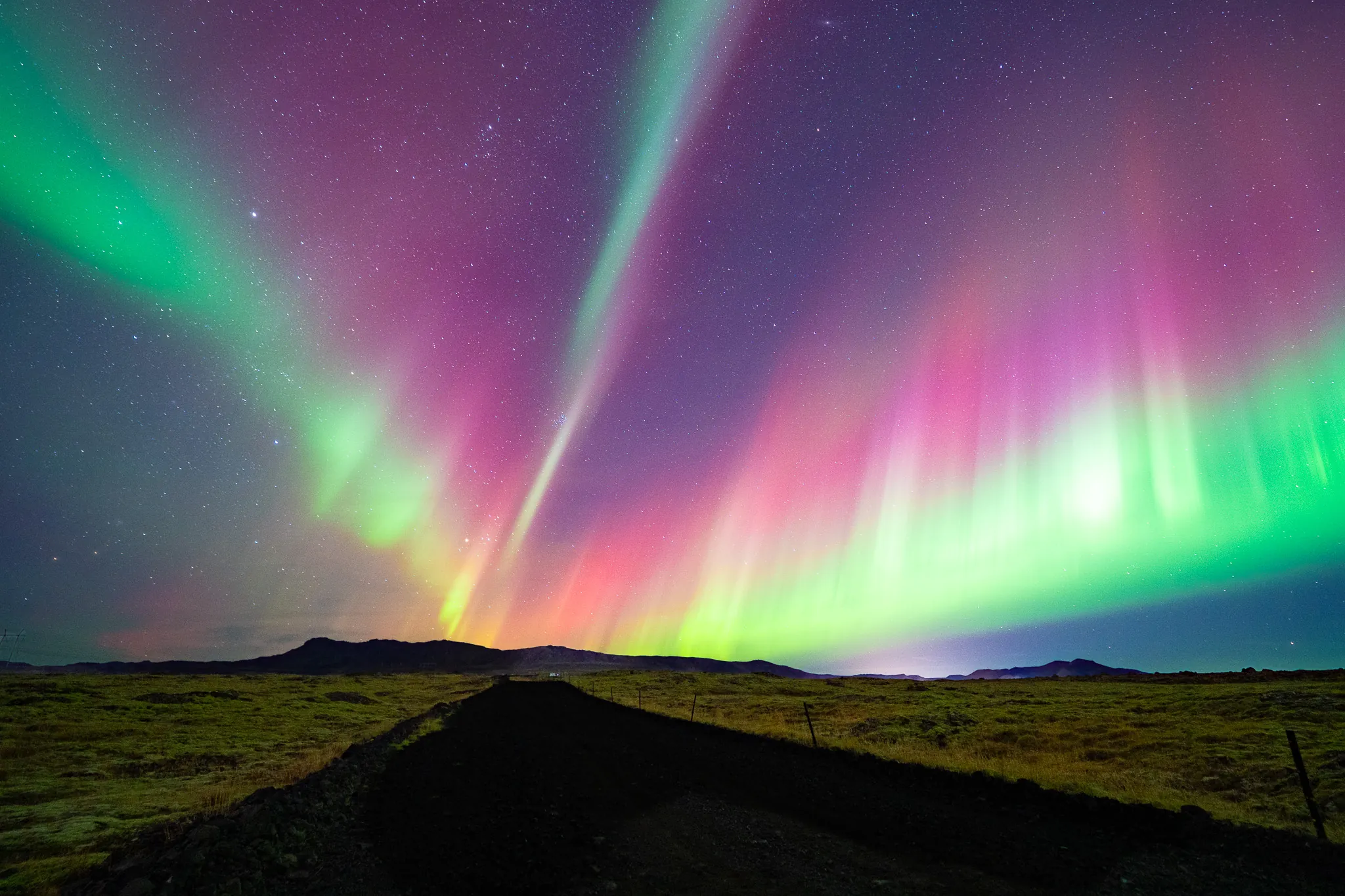 Broad curtains of green and pink aurora over an open Icelandic landscape