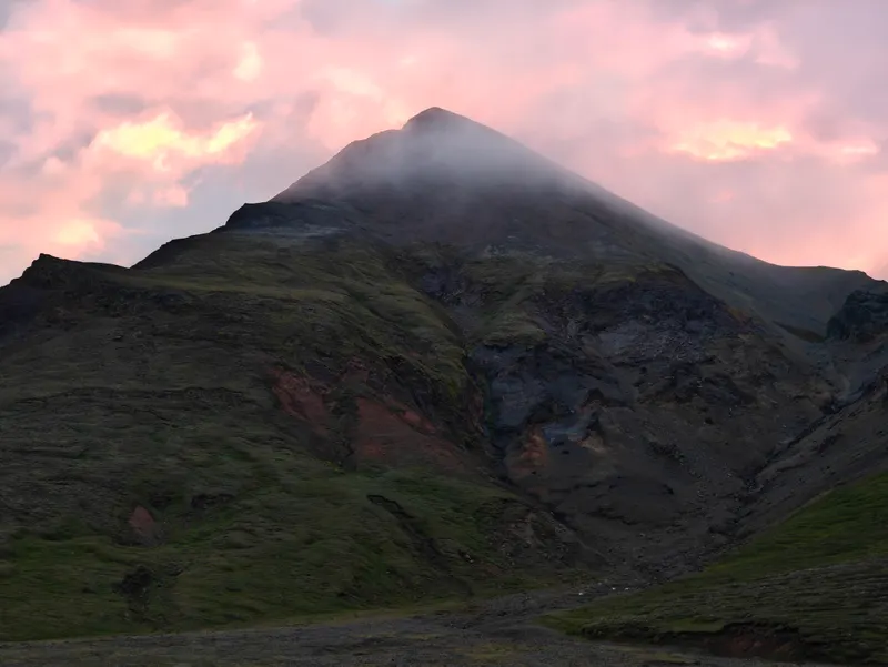 Pink evening clouds and wisps of mist above Rauðkollur mountain and the green slopes of Þjófadalir