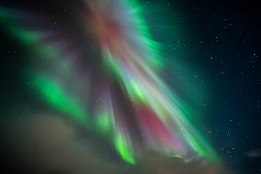 Green, pink and violet auroral rays spreading across a starry sky