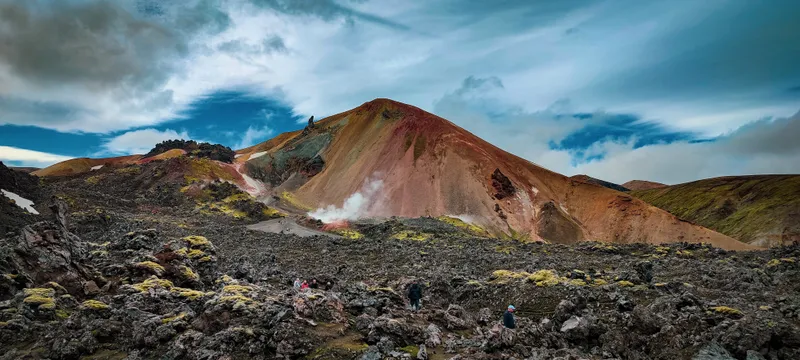 Dark lava and rising steam below the red and ochre slopes of Brennisteinsalda in Landmannalaugar