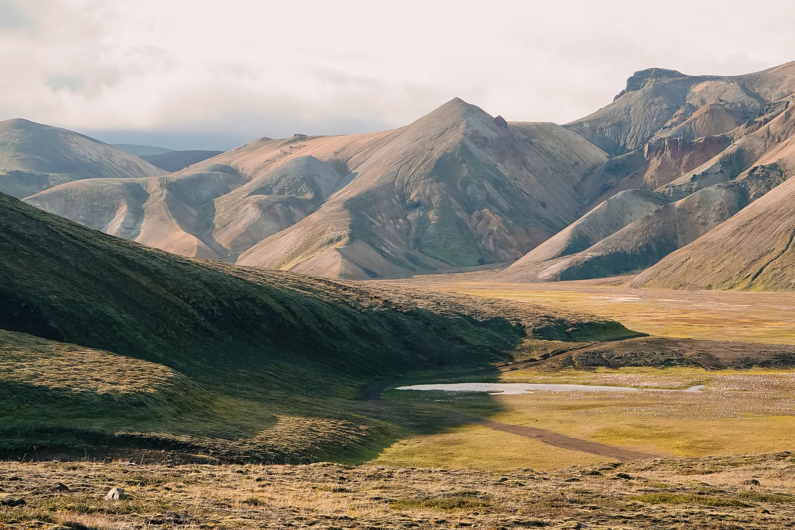 Layered rhyolite mountains above a grassy valley and winding stream in Landmannalaugar