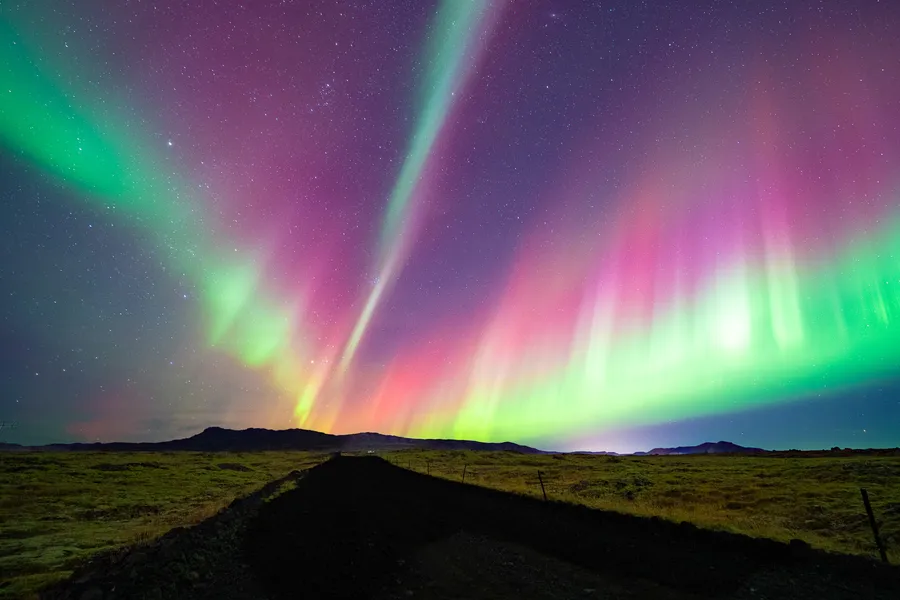 Pink and green northern lights above a quiet Icelandic road