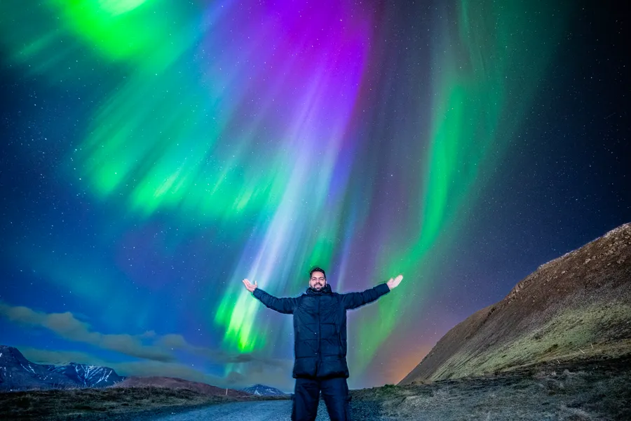 A guest standing with arms open beneath pink and green northern lights