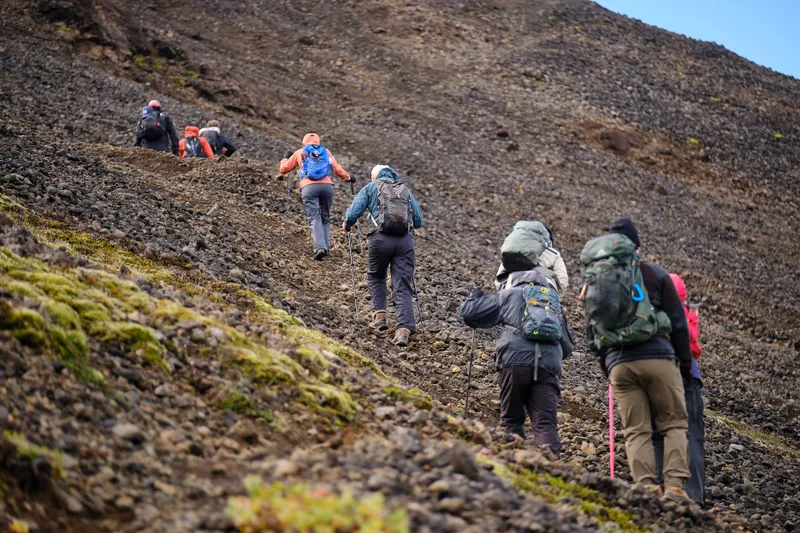 Hikers with trekking poles and daypacks climbing a steep slope covered in loose gravel